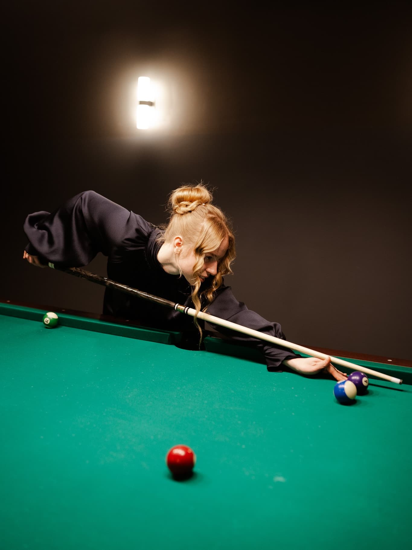 Woman lining up a shot over a billiard table in moody light
