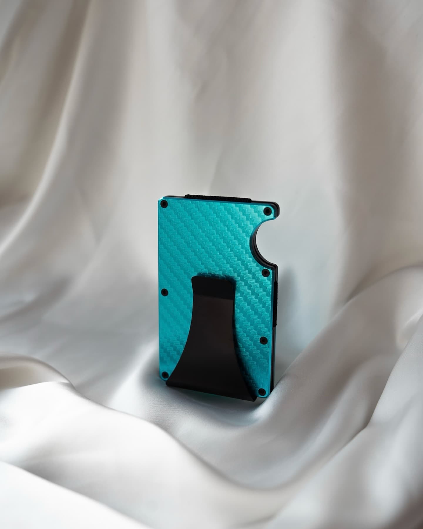 Product photo of a turquoise cardholder on white silk